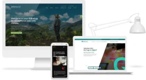 Drei digitale Geräte mit unterschiedlichen Website-Designs: Ein Desktop-Monitor zeigt eine B2B-Webshop-Startseite für Spezialitätenkaffee mit Naturhintergrund, ein Smartphone präsentiert eine mobile Ansicht mit Text und Bild einer Frau, ein Laptop zeigt eine Website mit Text „Verhalten führt. Die Frage ist: Wohin?“ und bunten Haftnotizen. Rechts daneben eine weiße Schreibtischlampe. Darstellung von Responsive Webdesign und professioneller Homepage.